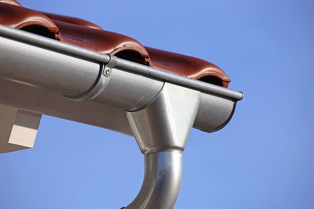 Gros plan sur une gouttière en zinc neuve et une descente d'eau pluviale.